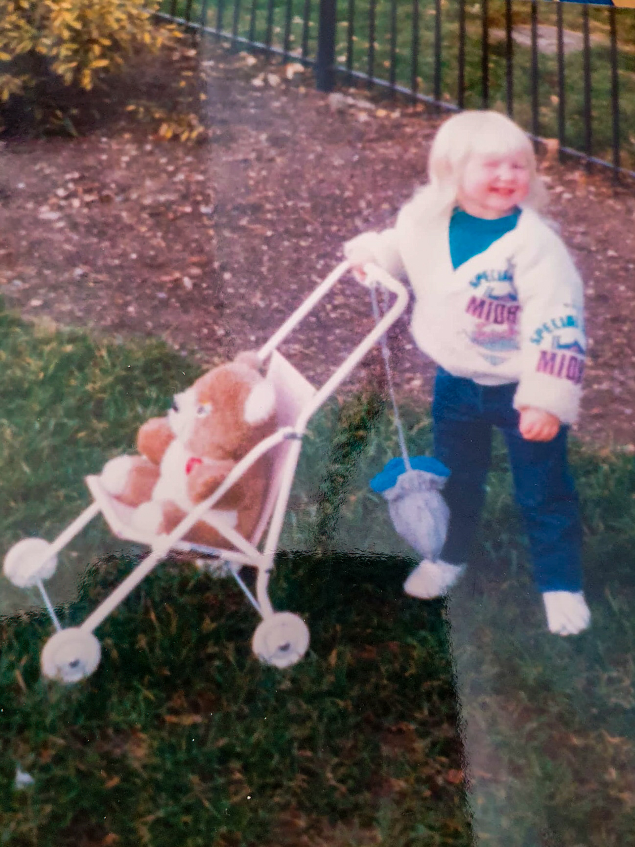 A young child with blond hair pushes a toy stroller holding a teddy bear.