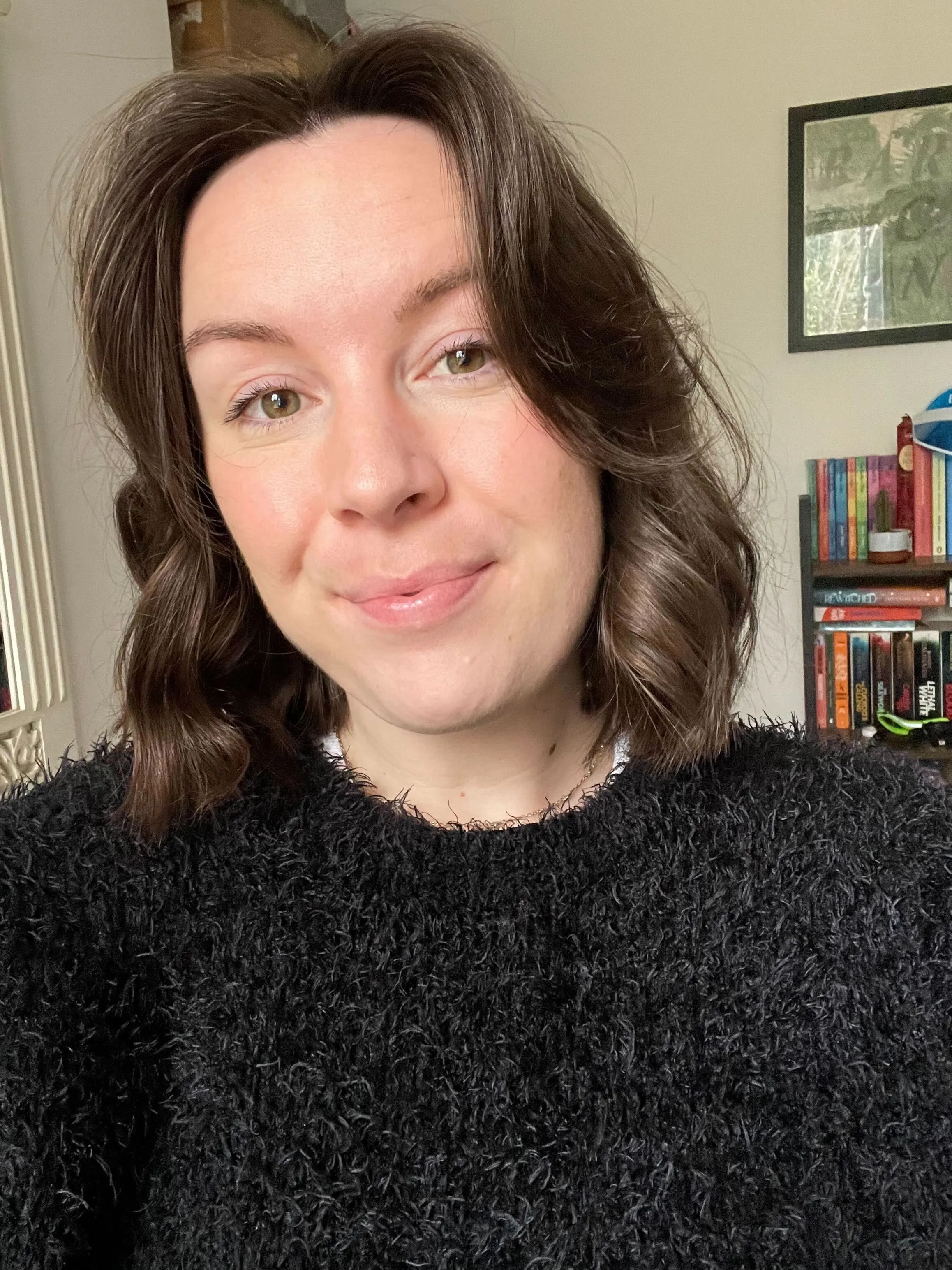 Woman with brown hair smiles softly, wearing a black fuzzy sweater.