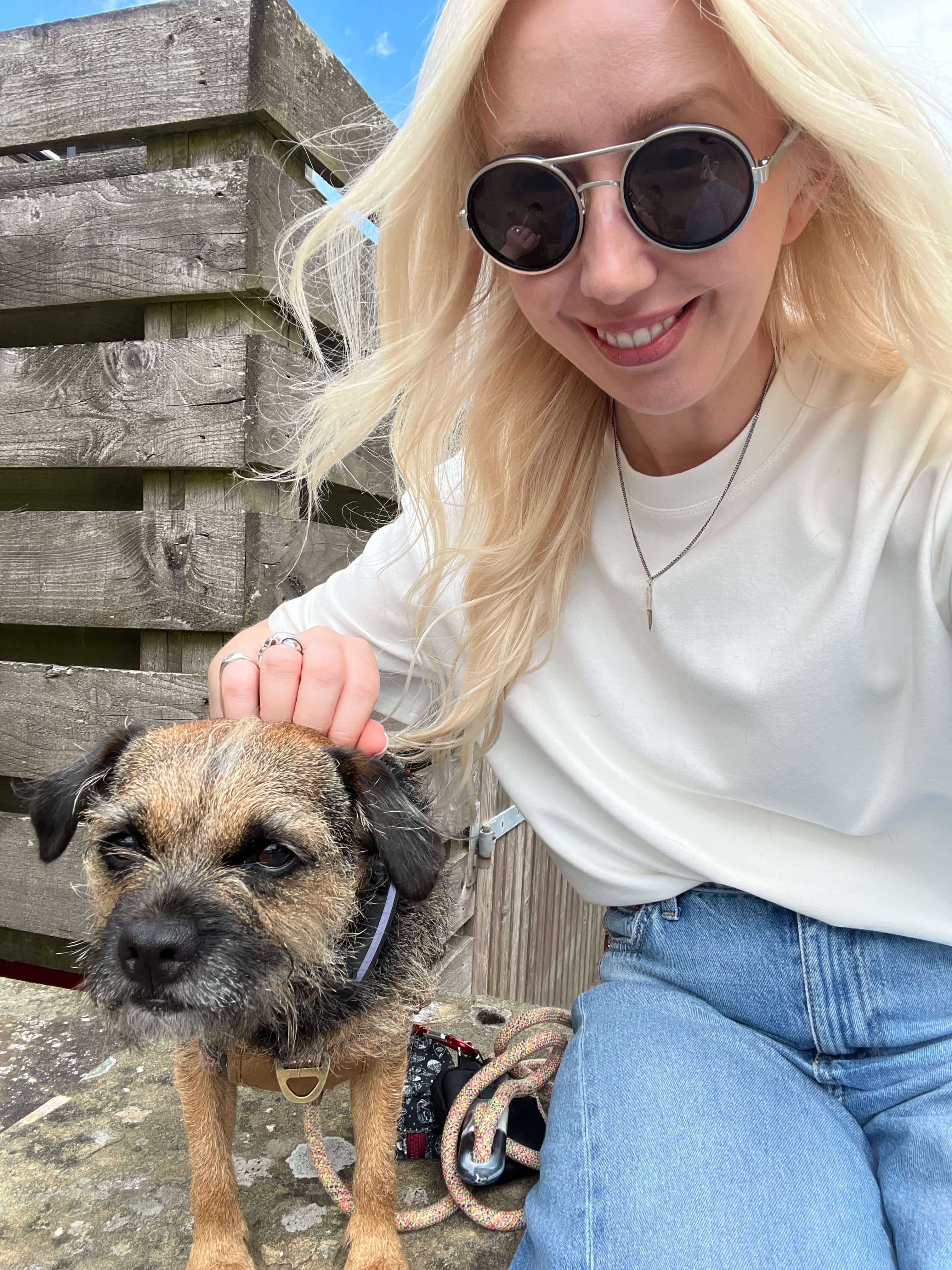 Smiling woman in sunglasses petting a small brown dog.