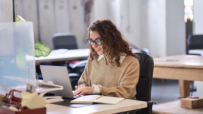 girl at desk working on laptop and writing notes