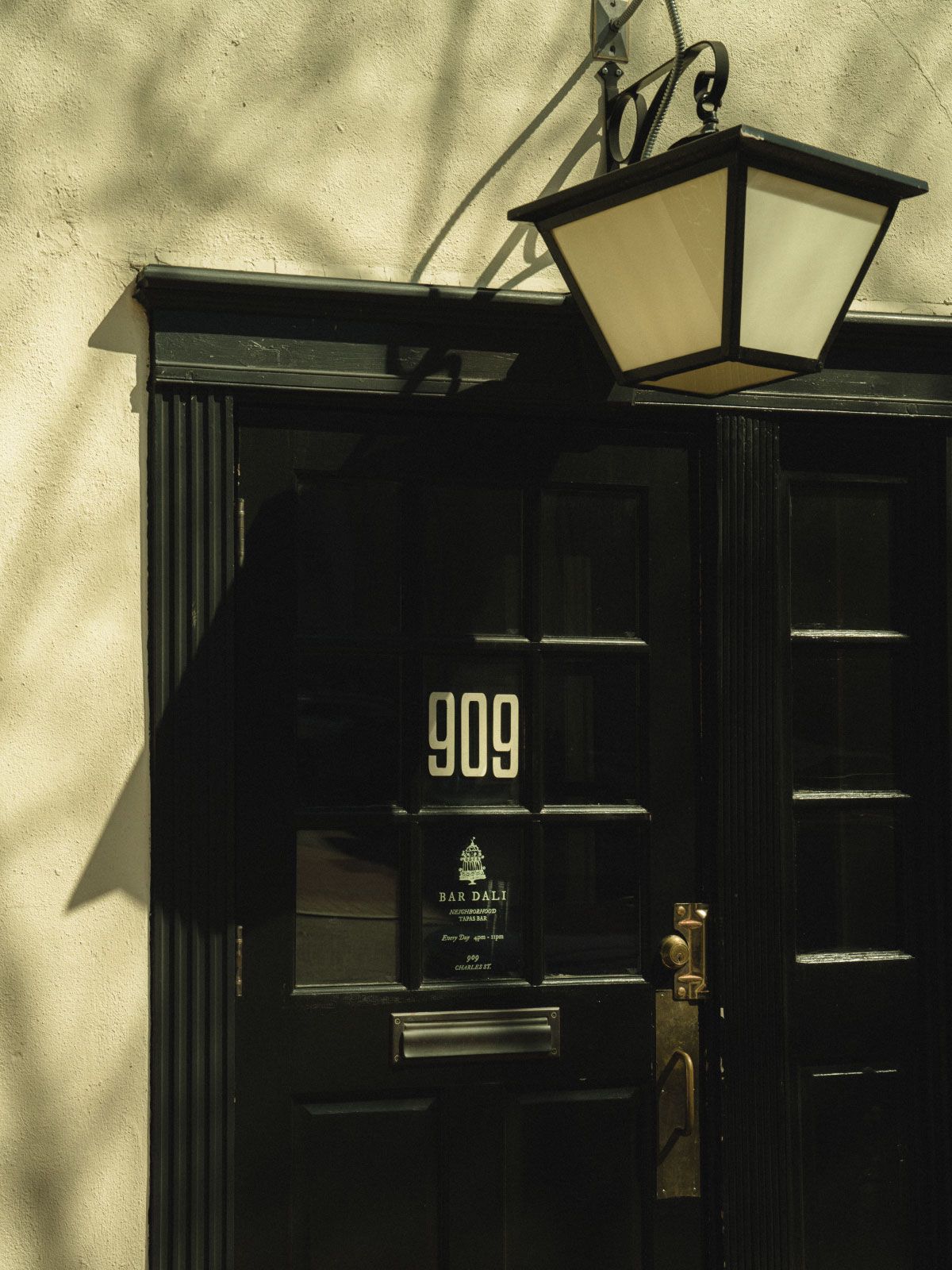 A black door with number 909, a sign for "Bar Dali," and a vintage lantern above, set against a cream-colored wall.