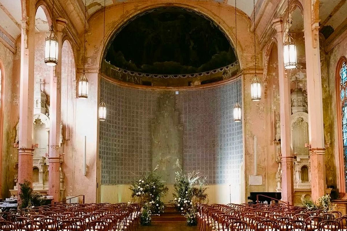 A beautifully decorated church interior with arched columns, hanging lanterns, and rows of wooden chairs facing an ornate altar.
