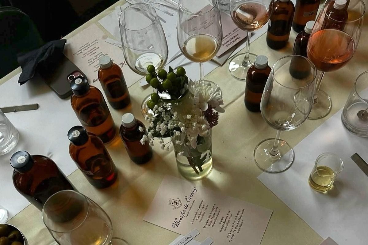 A table with wine glasses, amber bottles, a menu, and a vase of flowers set on a white tablecloth.