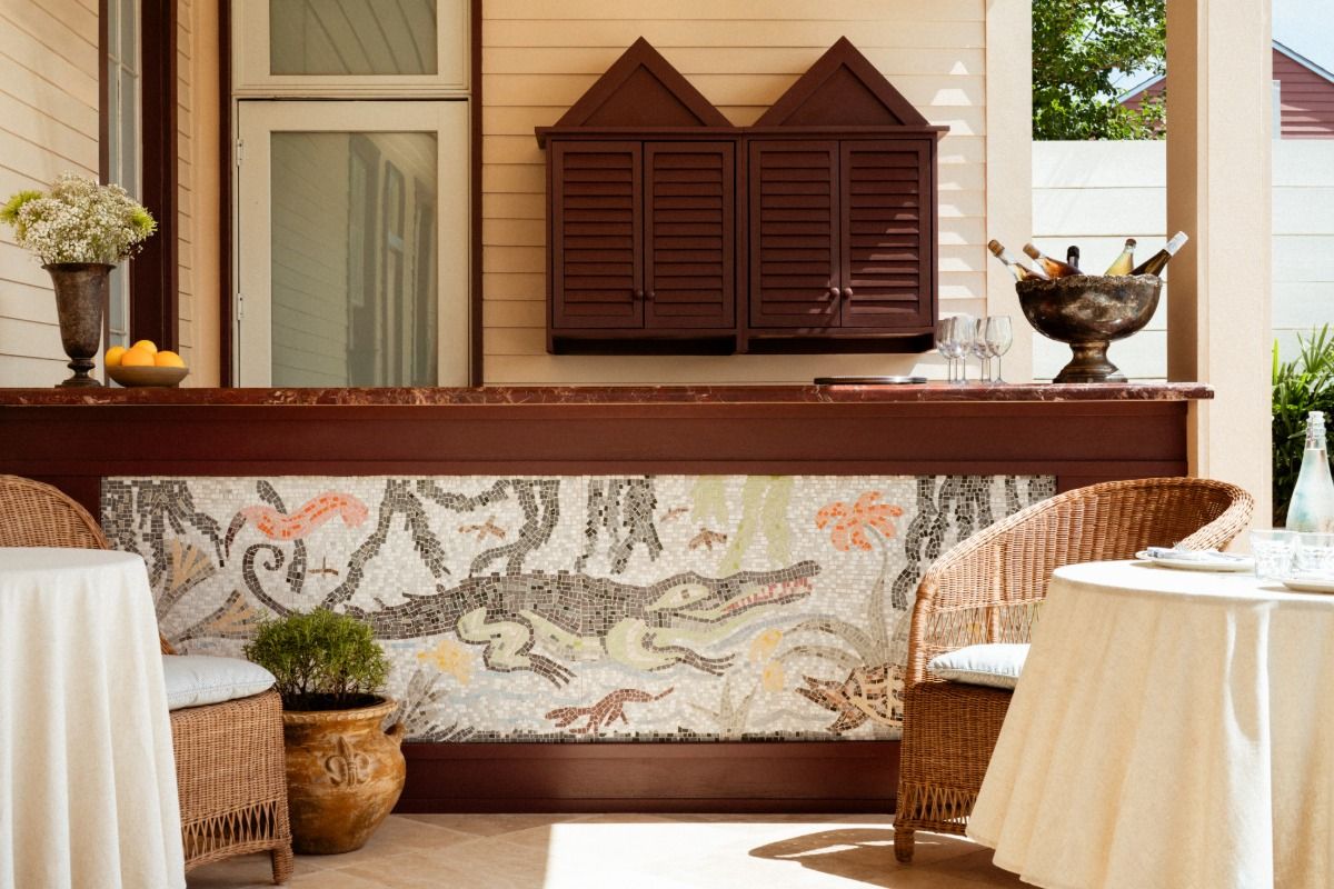 Outdoor patio with wicker chairs, a table, and a mosaic bar featuring a crocodile design. Wine bottles chill in an ice bucket on the counter.