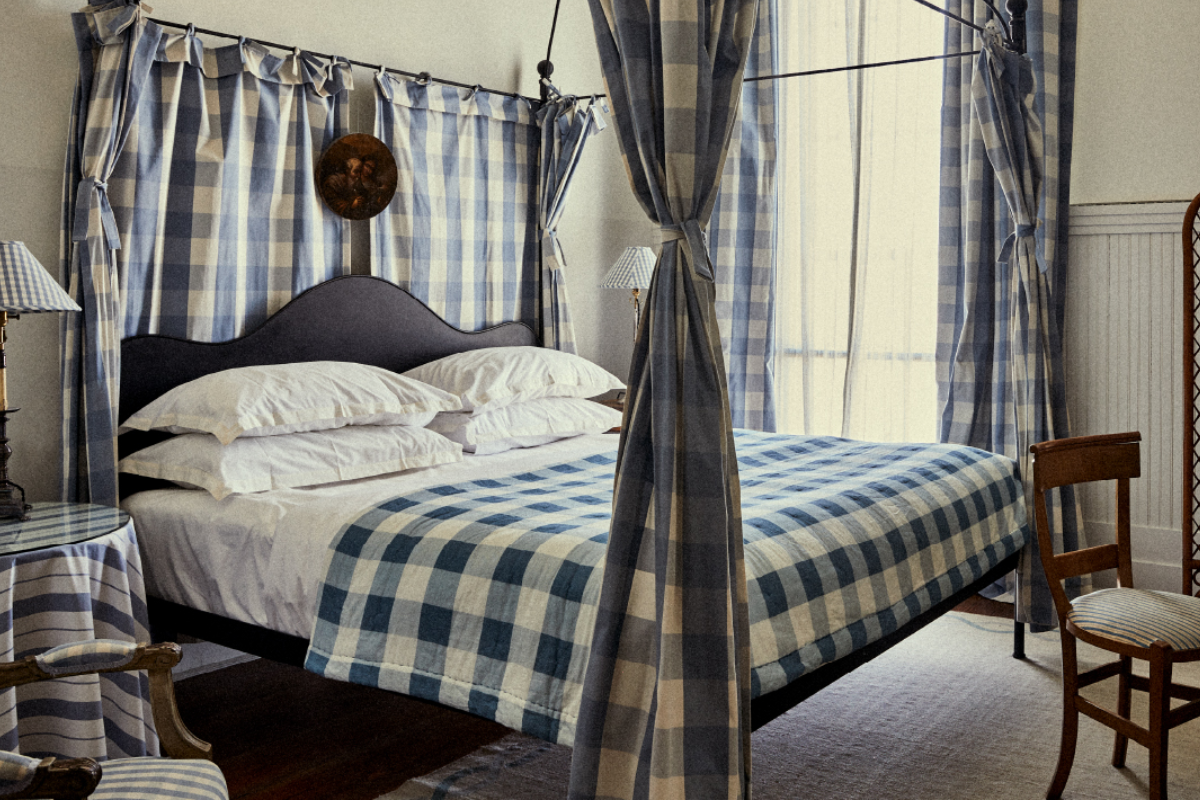 Cozy bedroom with a canopy bed draped in blue and white checkered fabric, wooden chair, and soft lighting from matching lampshades.