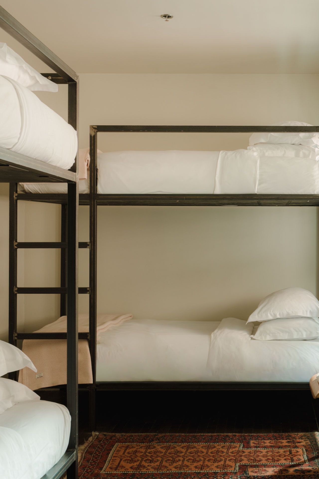 A room with two black metal bunk beds, white bedding, and a patterned rug on a dark wooden floor.