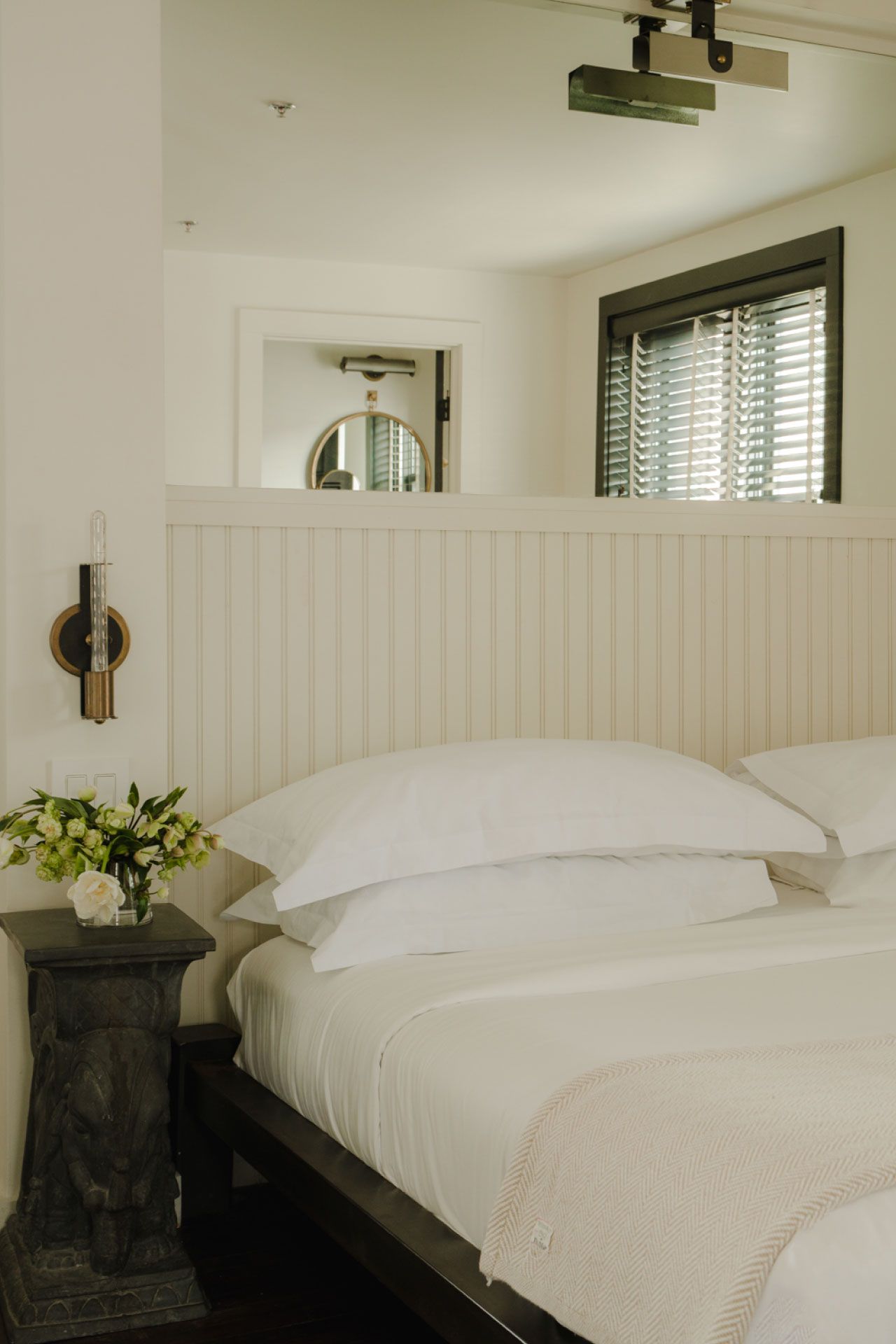 Cozy bedroom with a neatly made bed, white linens, an elephant-shaped bedside table, and a vase of fresh flowers.