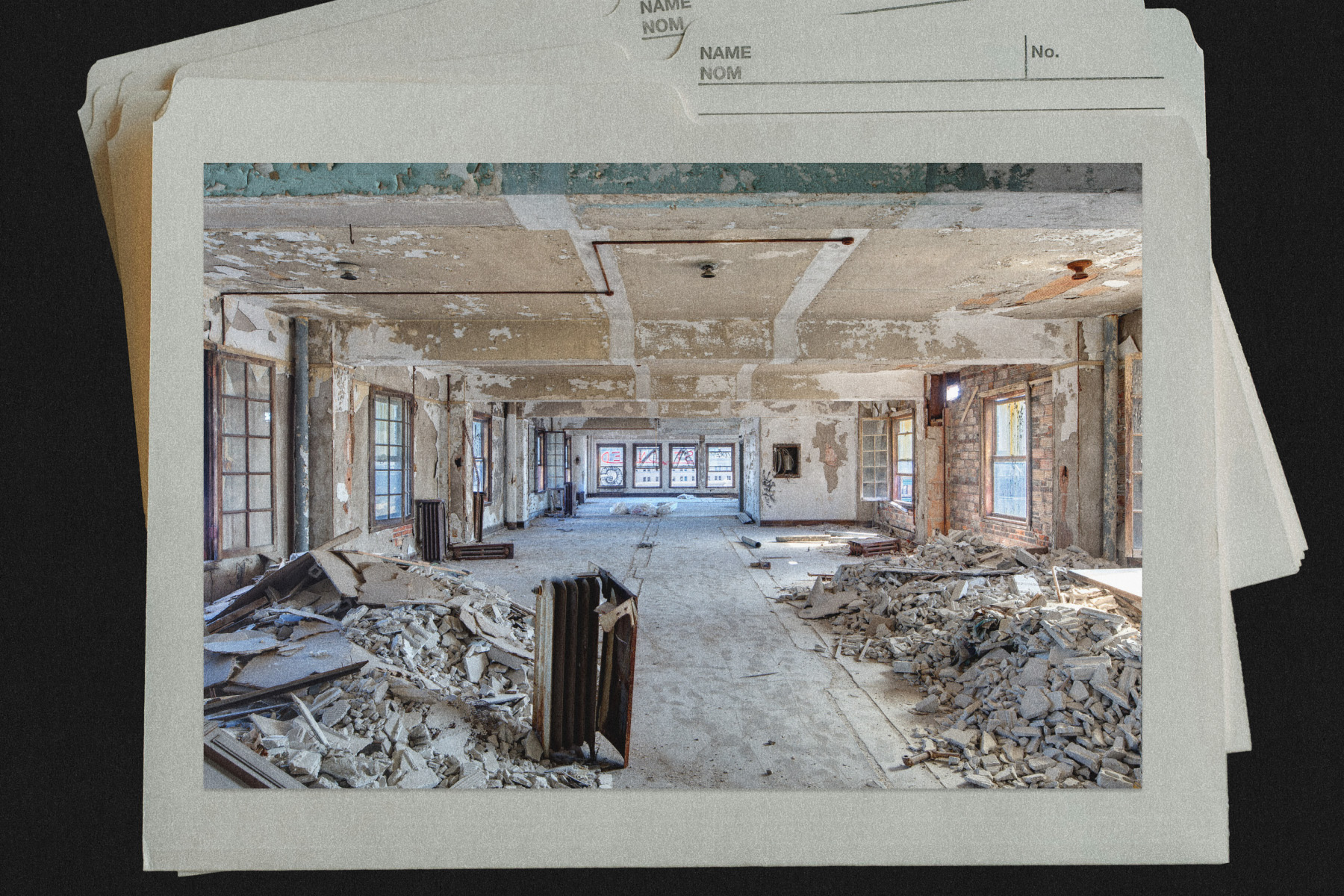 Interior of an abandoned building with peeling walls and debris scattered on the floor, featuring large windows and exposed structural elements.