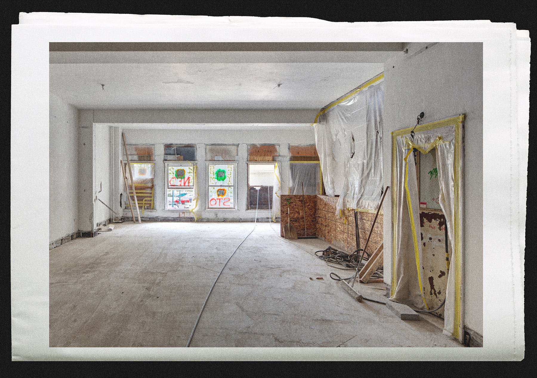 Empty room under renovation with plastic-covered windows, tools, and construction materials. Brightly painted windows in the background.