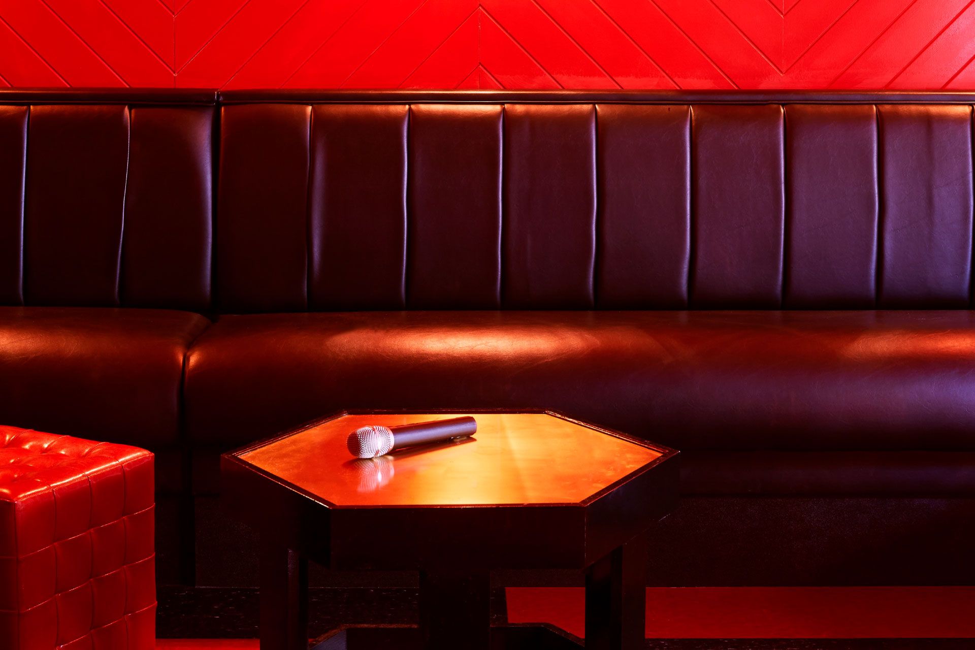 A microphone rests on a hexagonal wooden table in front of a dark leather sofa against a red herringbone-patterned wall.