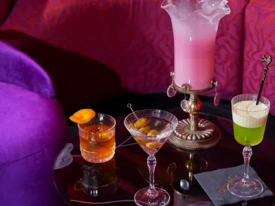 A variety of elegant cocktails on a round table with a purple chair and pink backdrop, featuring a decorative pink vase with ice.