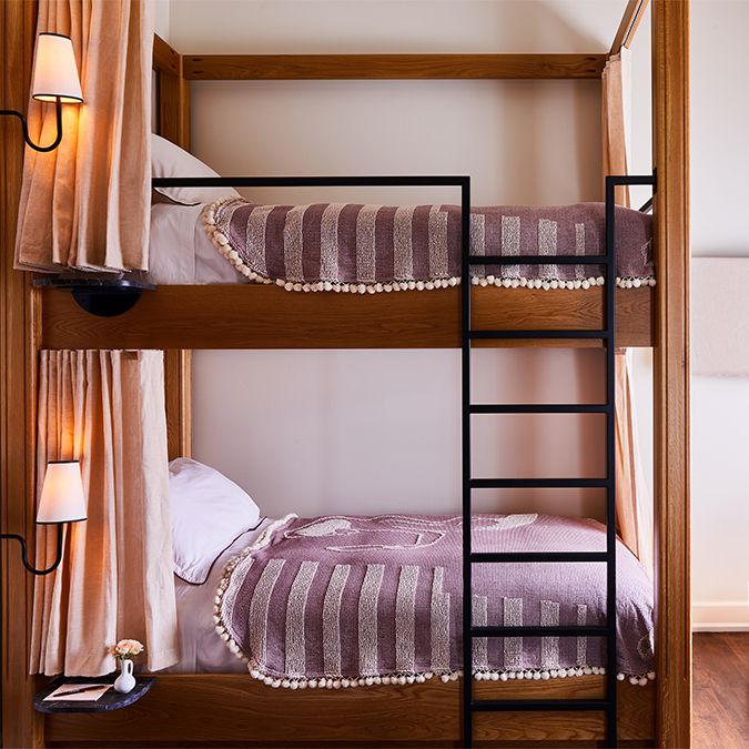 A cozy bunk bed with wooden frames, purple striped blankets, a black ladder, and soft lighting from sconces on the side.