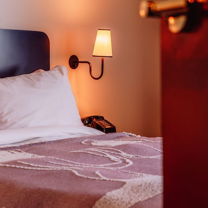 Cozy hotel room with a neatly made bed, a bedside lamp, and a telephone. Warm lighting creates an inviting atmosphere.