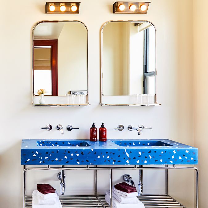 Double vanity with vibrant blue terrazzo countertop, two mirrors, chrome fittings, and neatly folded towels on the shelf below.