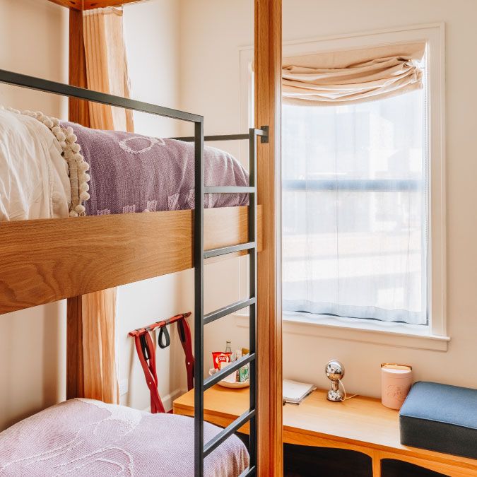Cozy room with bunk beds, a wooden desk, decorative items, and a window with sheer curtains letting in natural light.