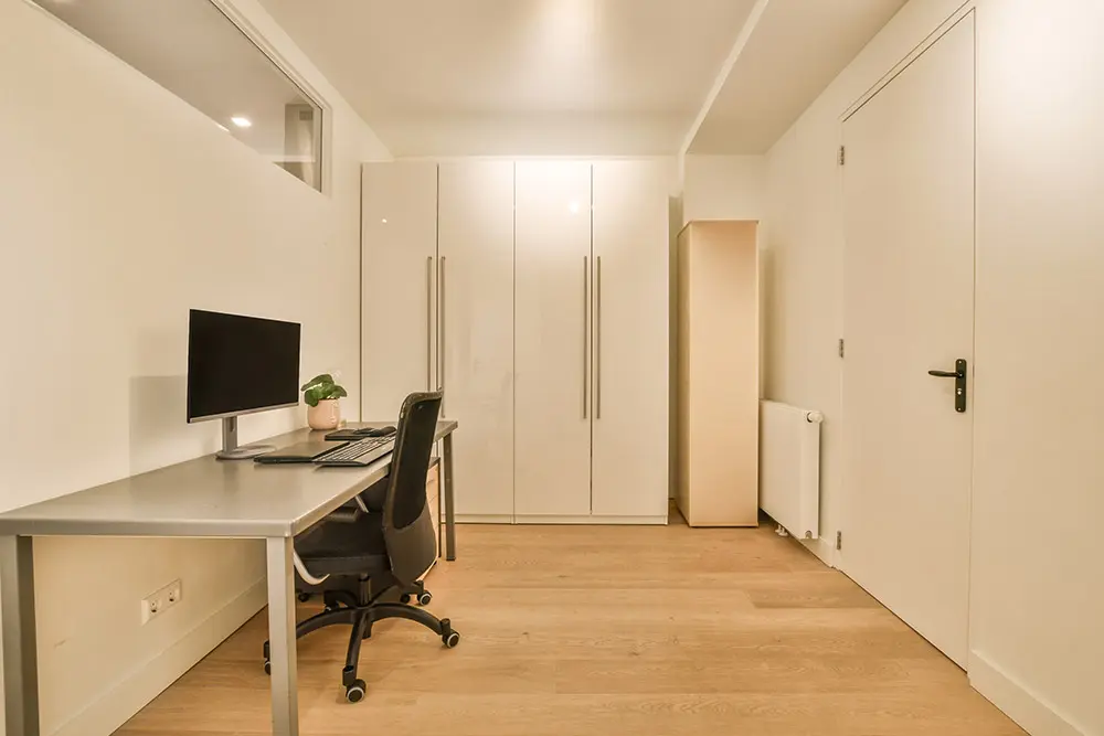 Ein minimalistisch eingerichtetes Homeoffice in einem Kellerraum mit Schreibtisch, Computer und Bürostuhl. 