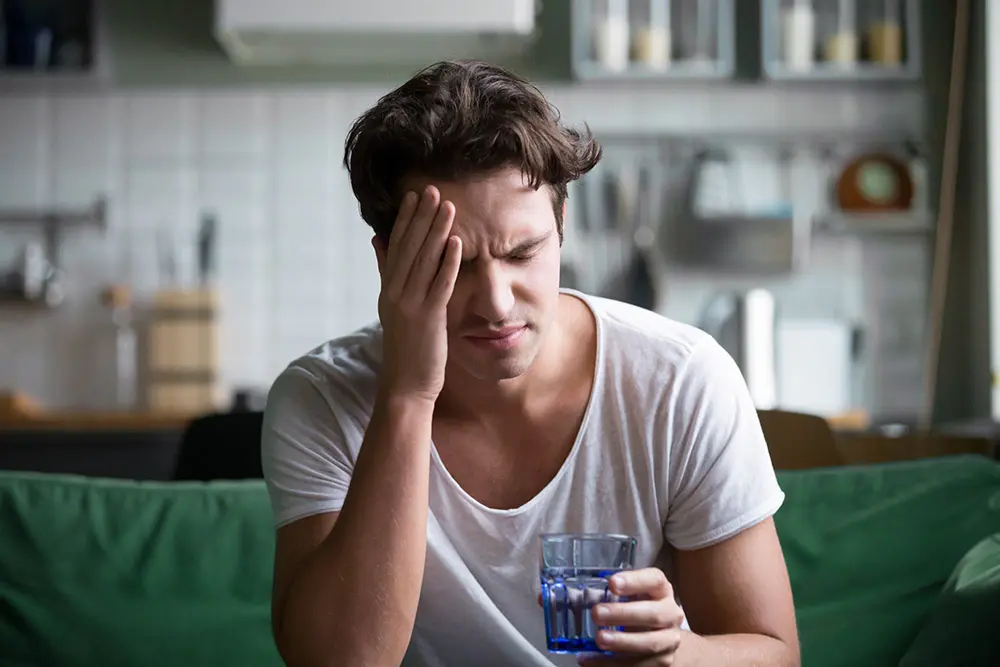 Ein junger Mann mit Kopfschmerzen hält sich den Kopf, was mögliche Symptome einer Radonbelastung symbolisiert.