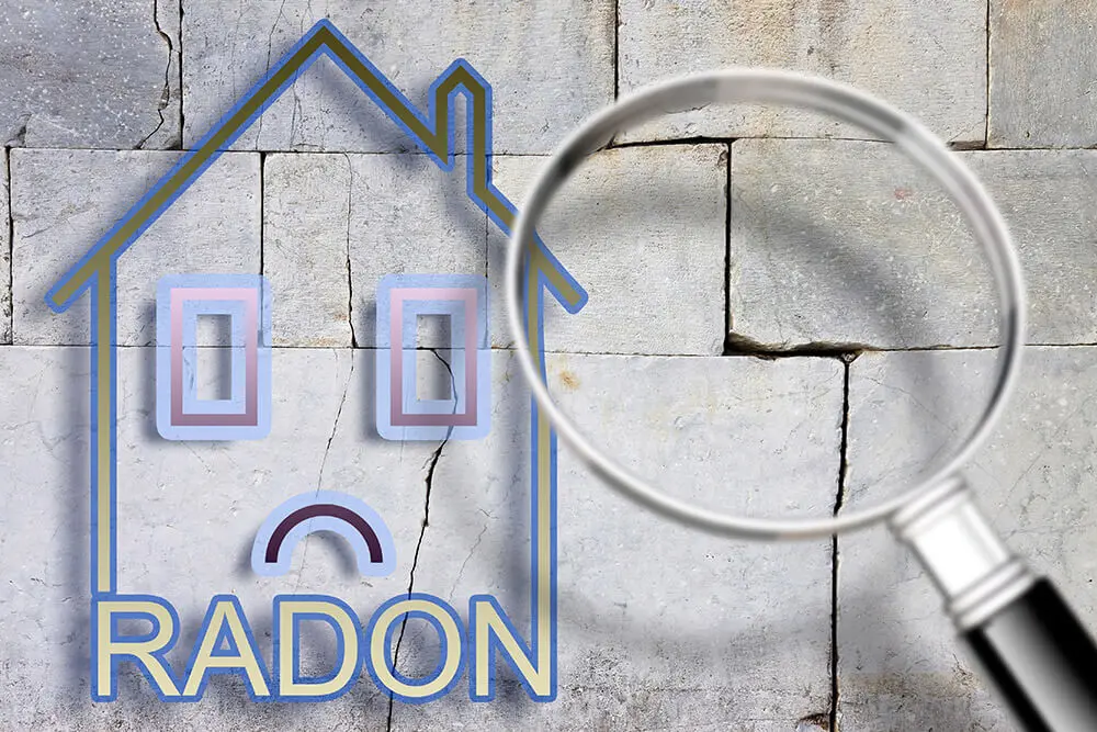 Symbolisches Haus mit traurigem Gesicht und dem Wort "Radon" auf einer Wand mit Rissen.