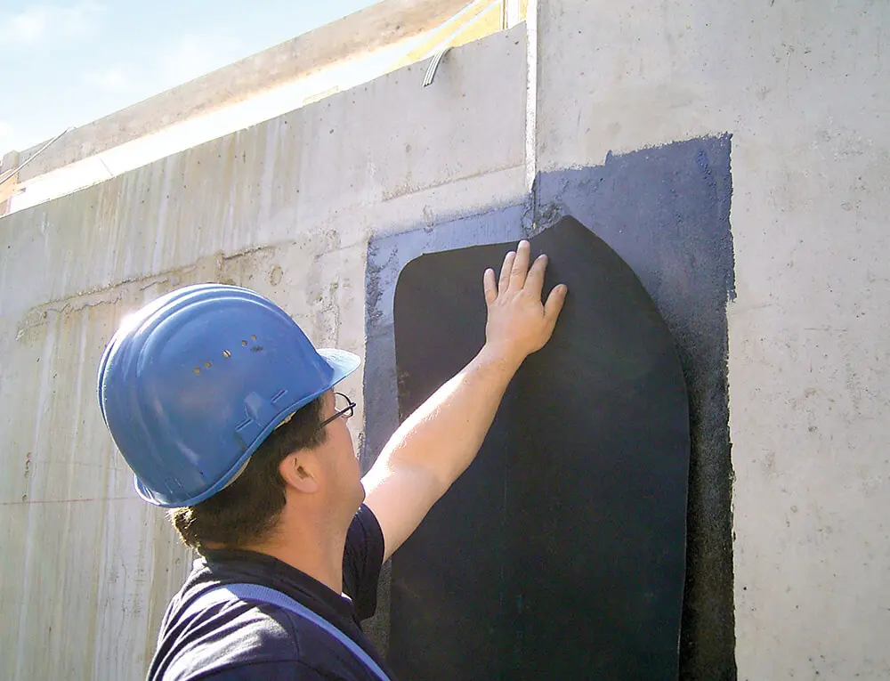 Handwerker dichtet eine Sollrissfuge in einer Kellerwand mit EPDM-Abdichtungsbahn ab 