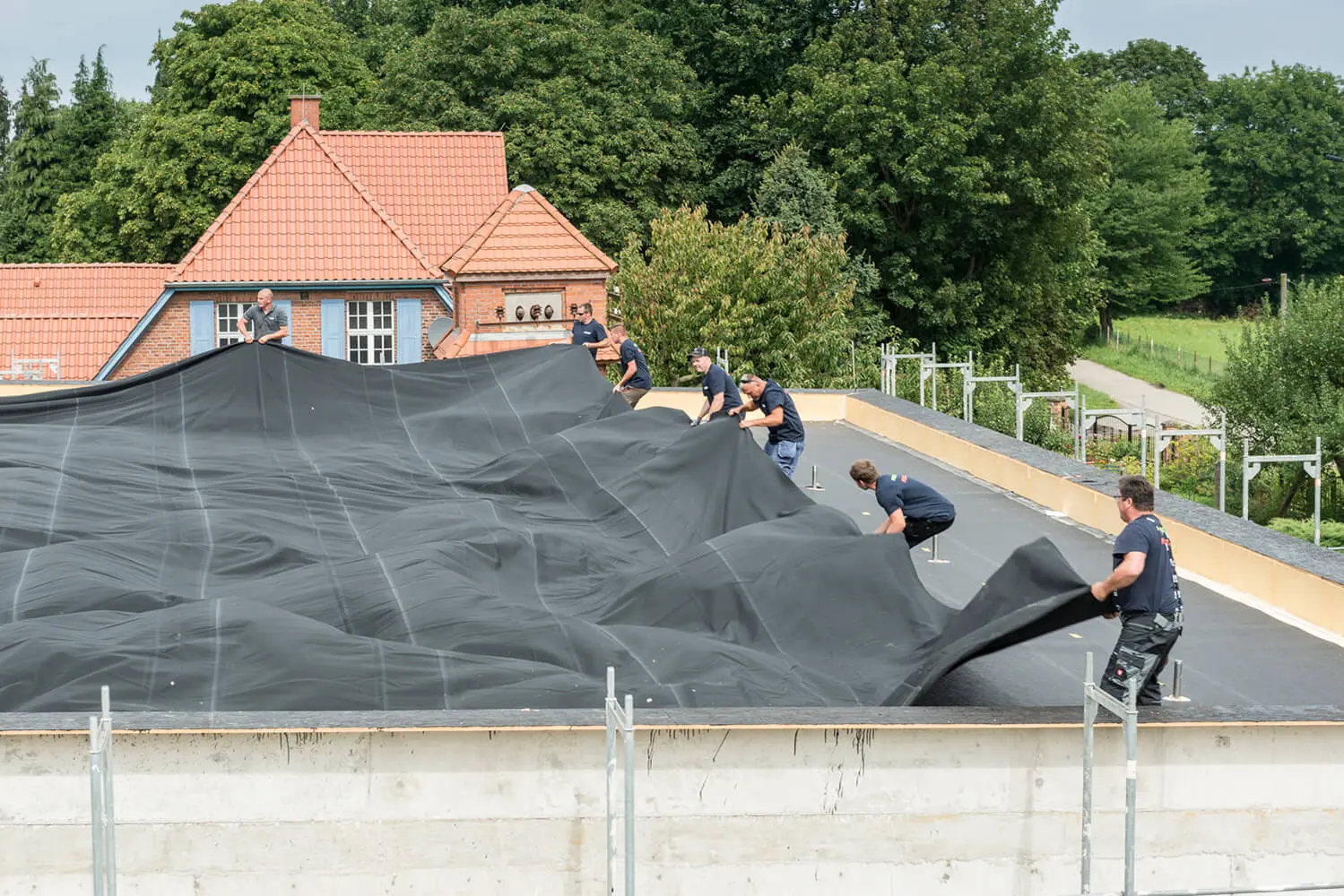 Verarbeiter verlegen eine großflächige HERTALAN EPDM-Plane auf einem Flachdach
