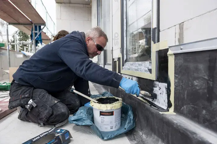 Arbeiter dichtet EPDM Wandanschluss auf Terrasse ab