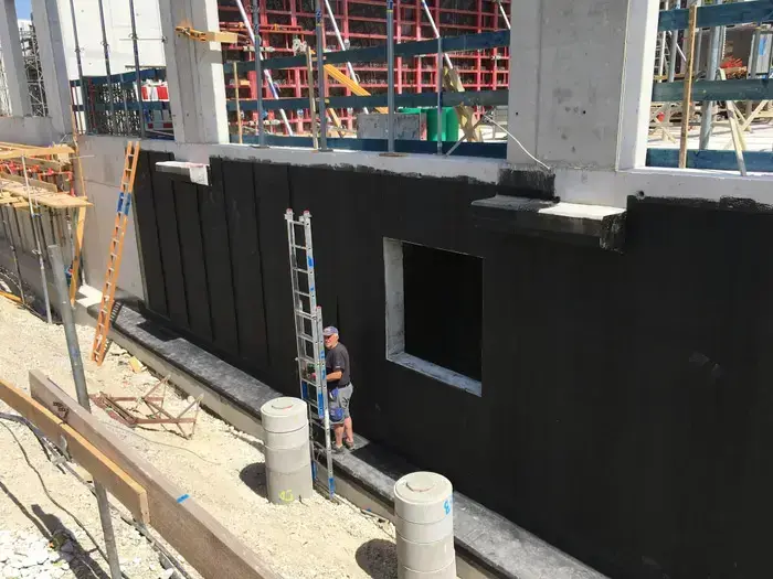 Bauarbeiter neben einer mit Radonabdichtung versehenen Betonwand als baulicher Strahlenschutz