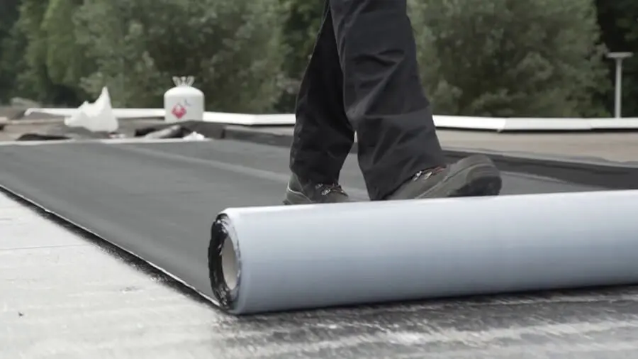 Person, die eine Abdichtungsbahn auf einem Flachdach ausrollt, um EPDM auf EPDM zu kleben.