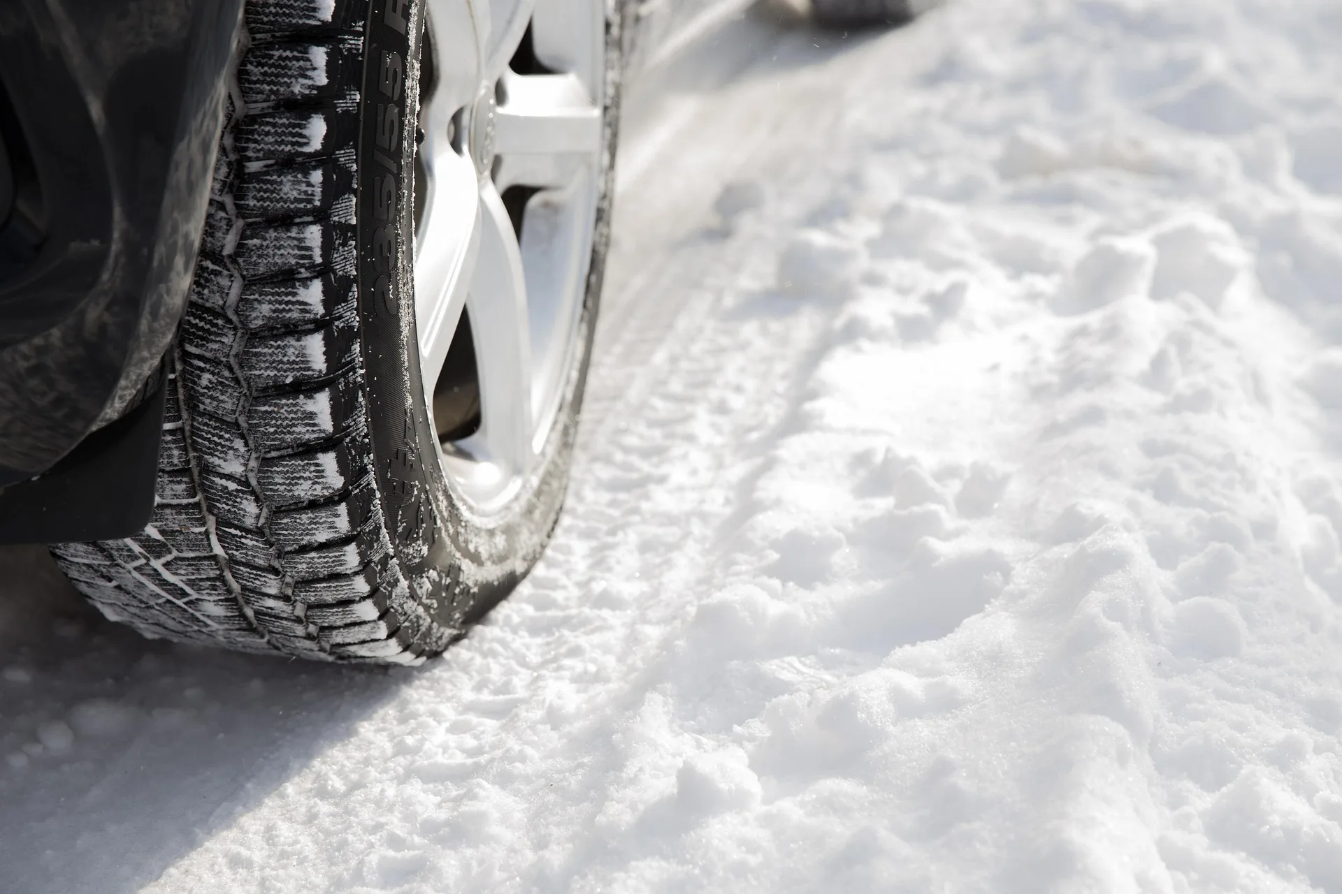 Close-up of a winter tyre with deep tread blocks and siping gripping packed snow