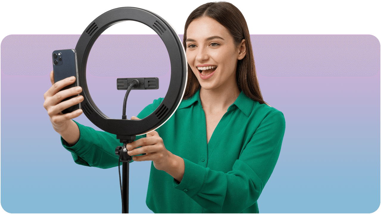 Woman in green shirt smiling at smartphone on tripod with ring light, against a pink and blue gradient background.