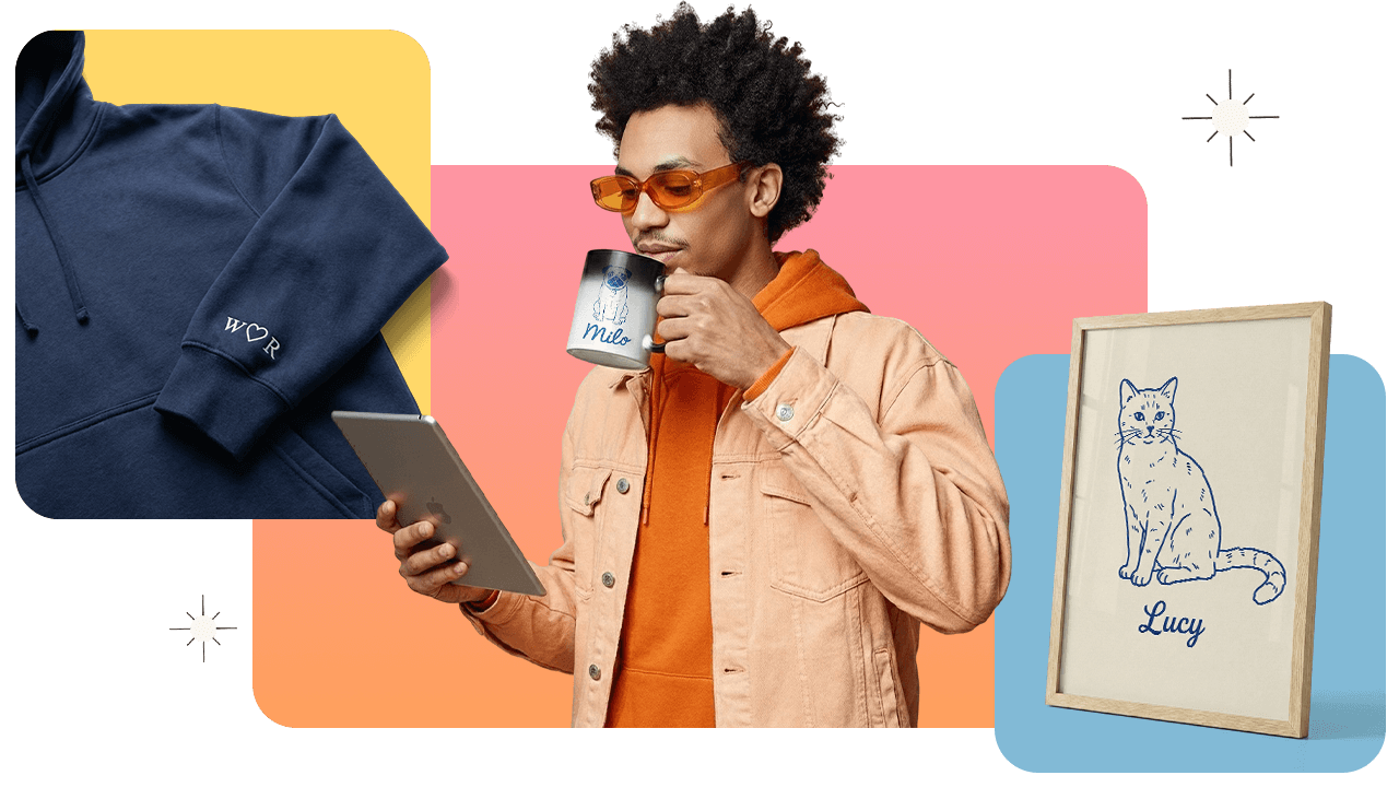 Young man in glasses drinks from a personalized mug while holding a tablet, with a hoodie and framed cat drawing nearby.