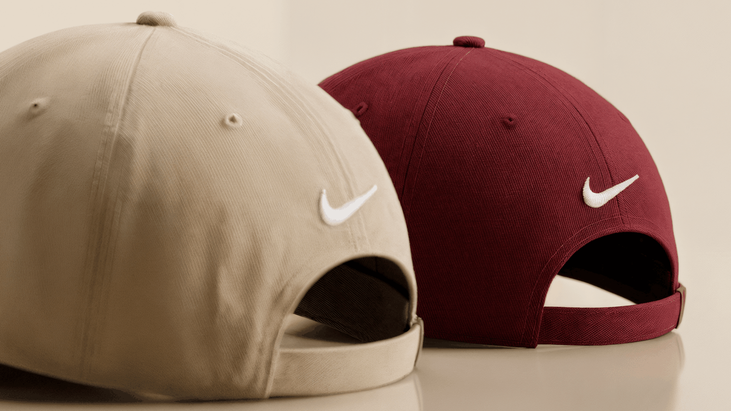 Back view of two baseball caps, beige and maroon, with white Nike swooshes and adjustable straps.
