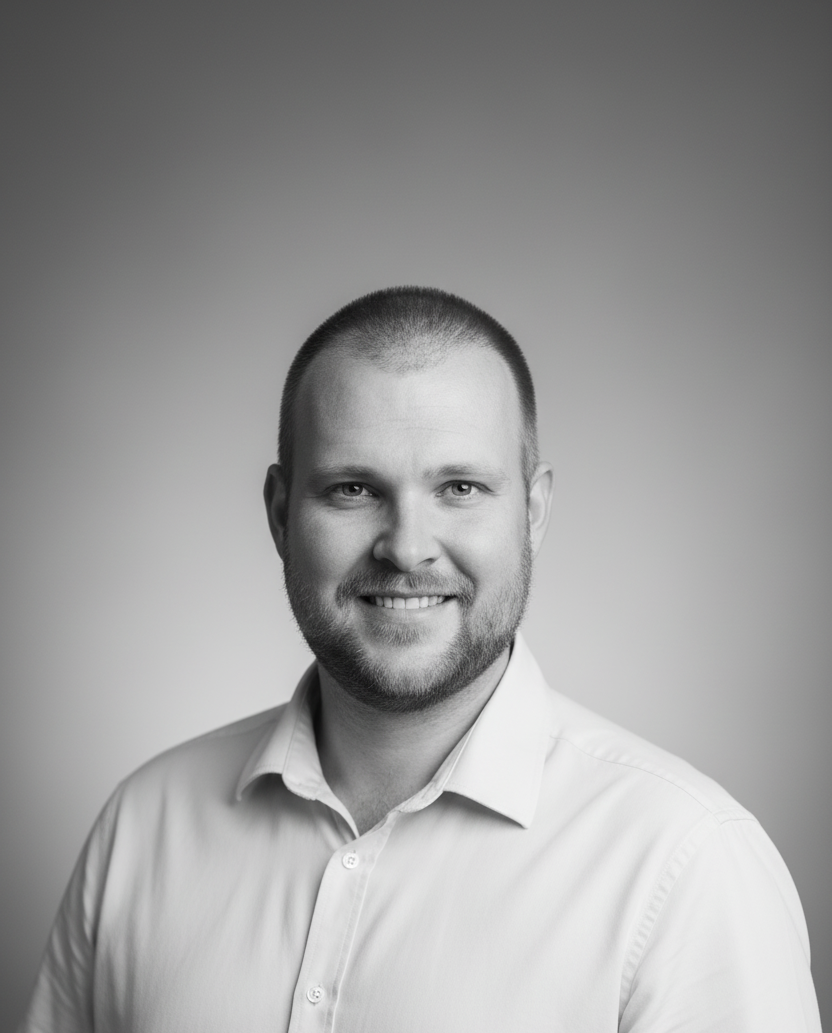 Smiling man with short hair and a beard, wearing a light-colored shirt, against a plain background. Black and white portrait.