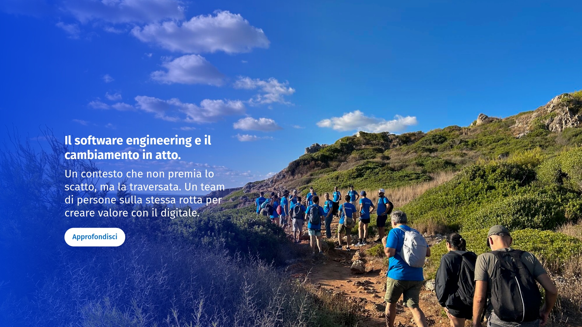A group of people hiking on a rocky trail under a blue sky with scattered clouds, surrounded by green hills.