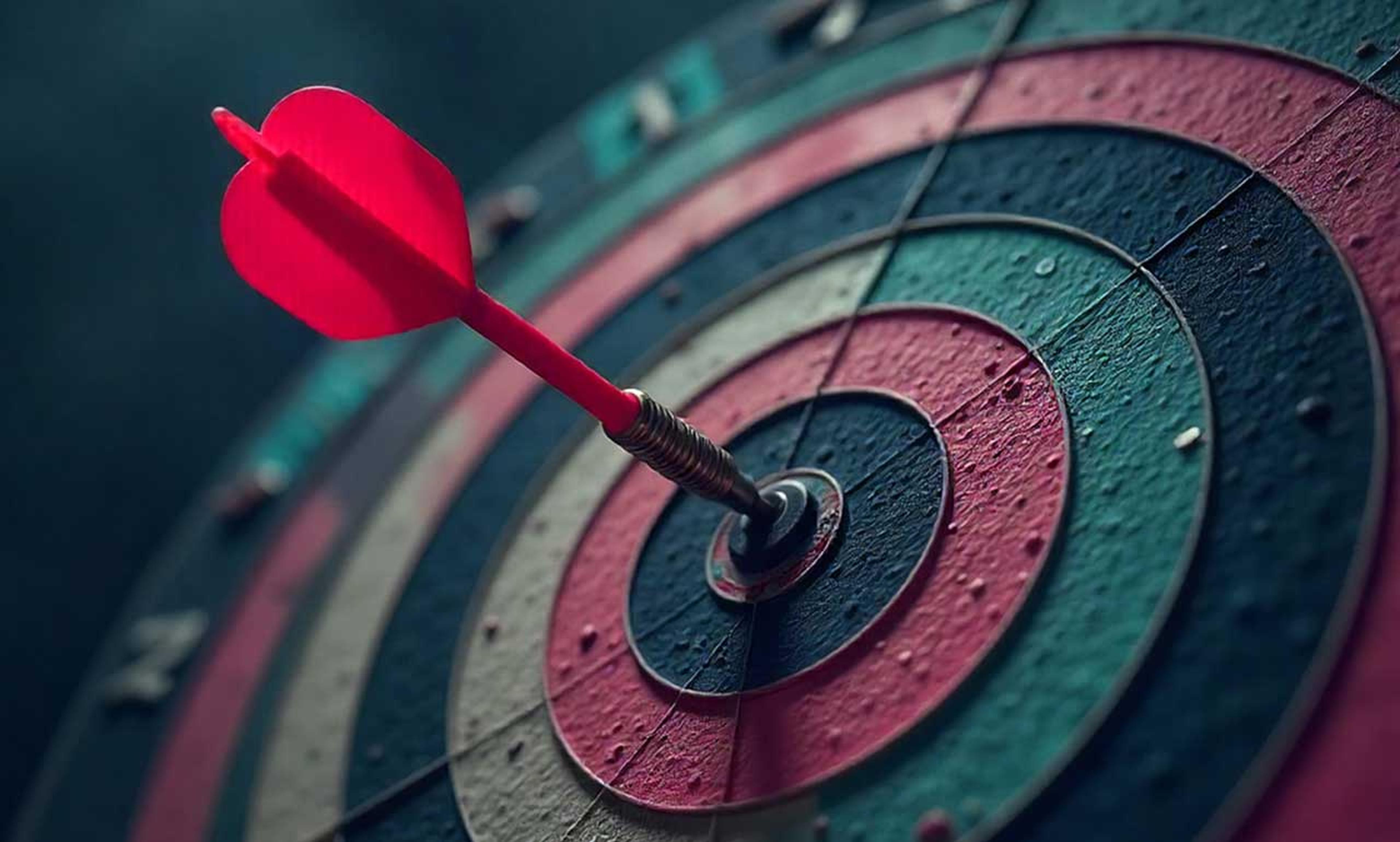 Nahaufnahme einer Dartscheibe mit einem roten Pfeil, der das Bullseye trifft