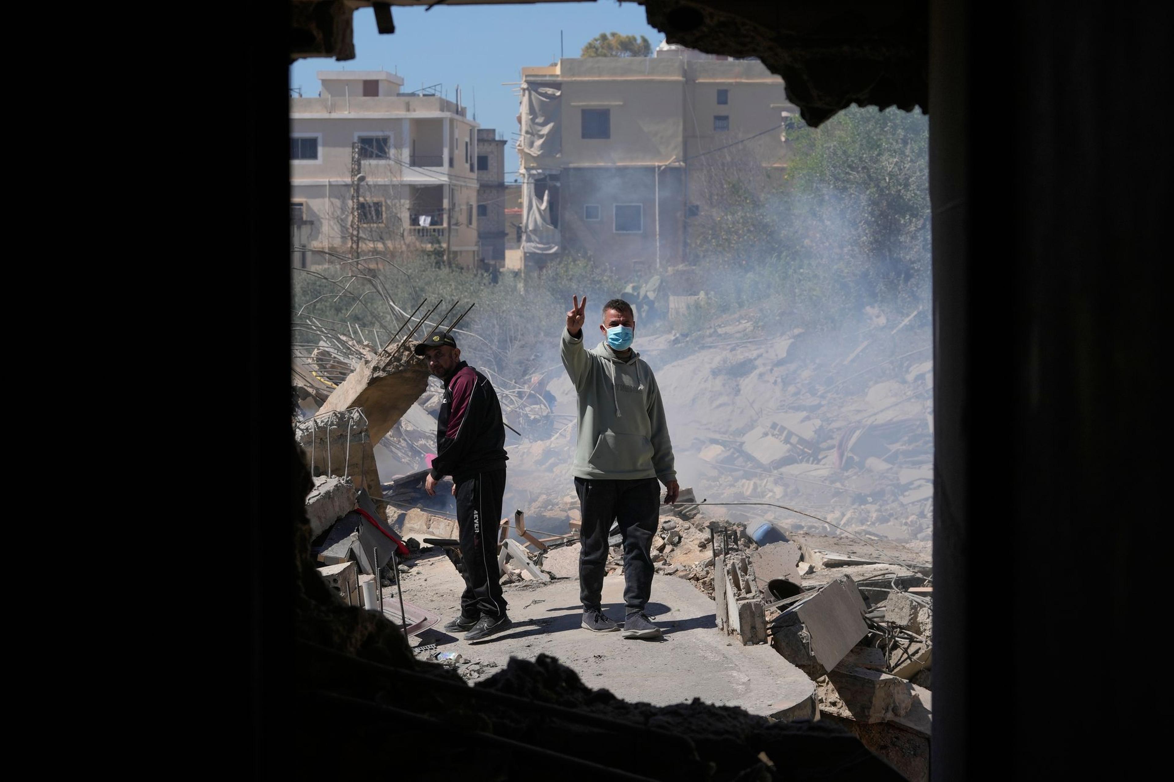 Ein Mann zeigt ein Siegeszeichen, während er auf den Trümmern seines zerstörten Hauses steht.