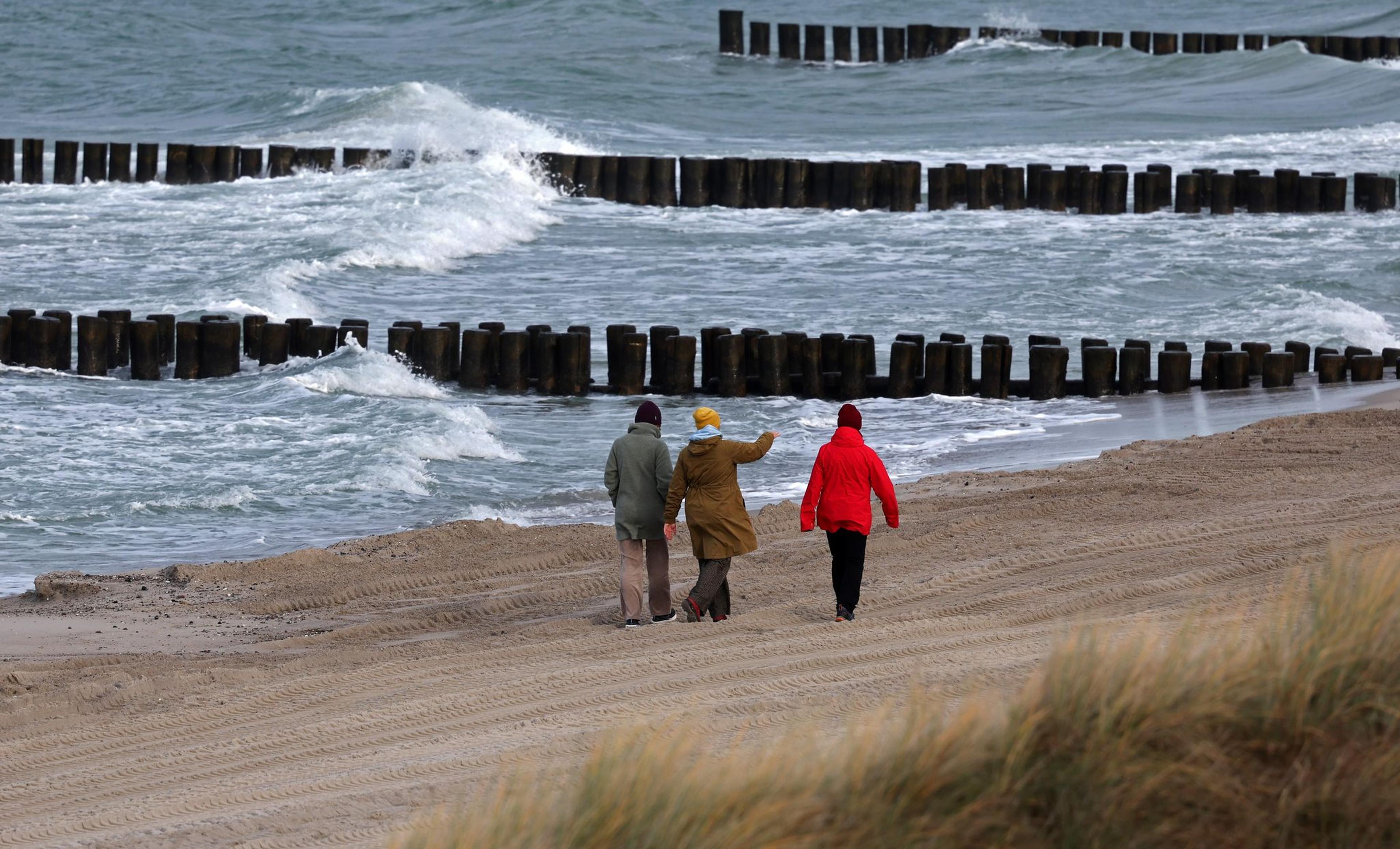 Spaziergänger sind am Ostseestrand unterwegs. Wind und Wolken dominieren das Wetter im Norden.