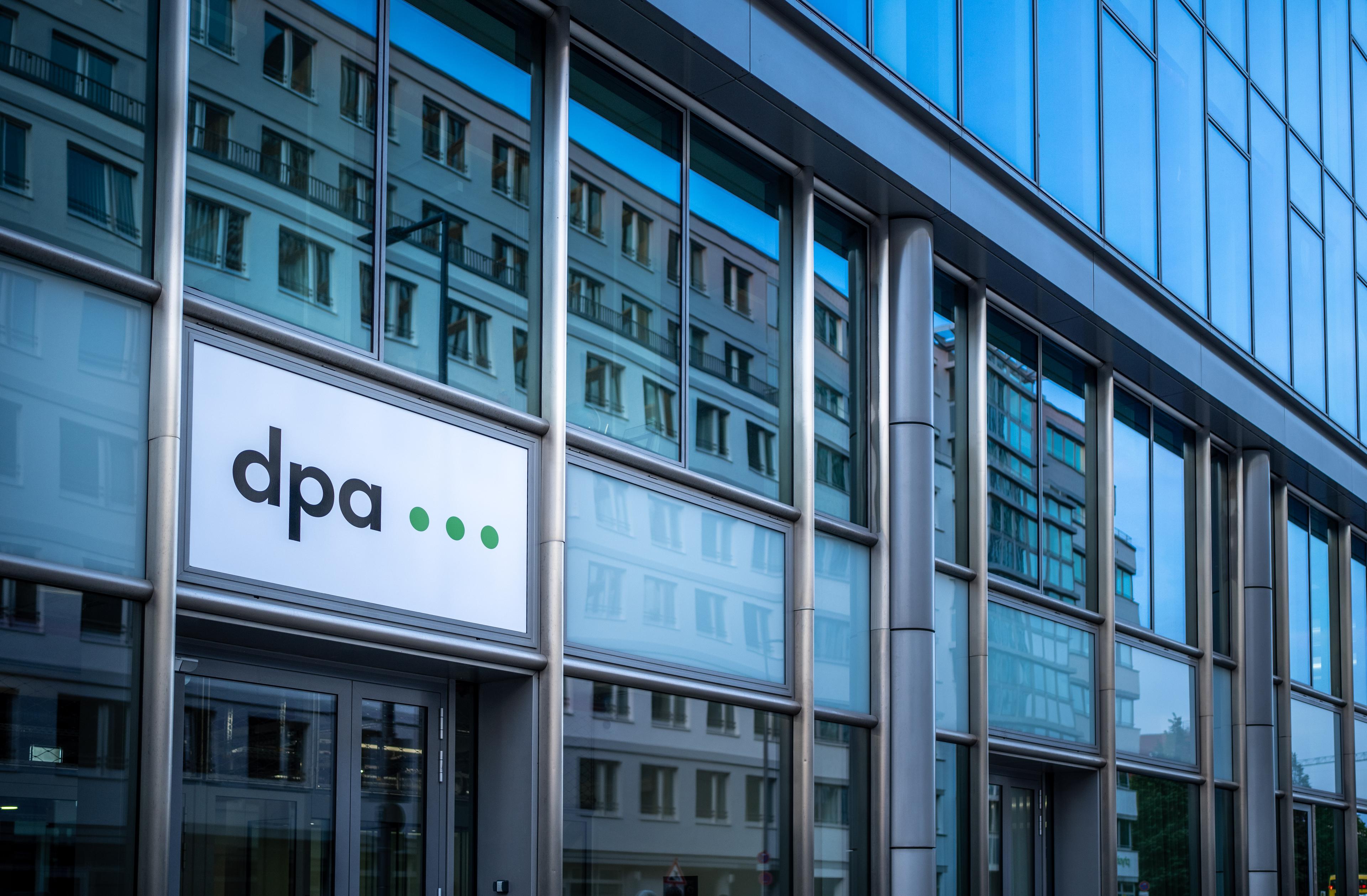 Eine Außenaufnahme des dpa-Newsrooms in Berlin. Gebäude spiegeln sich im Glas, das dpa-Logo steht im Fokus.