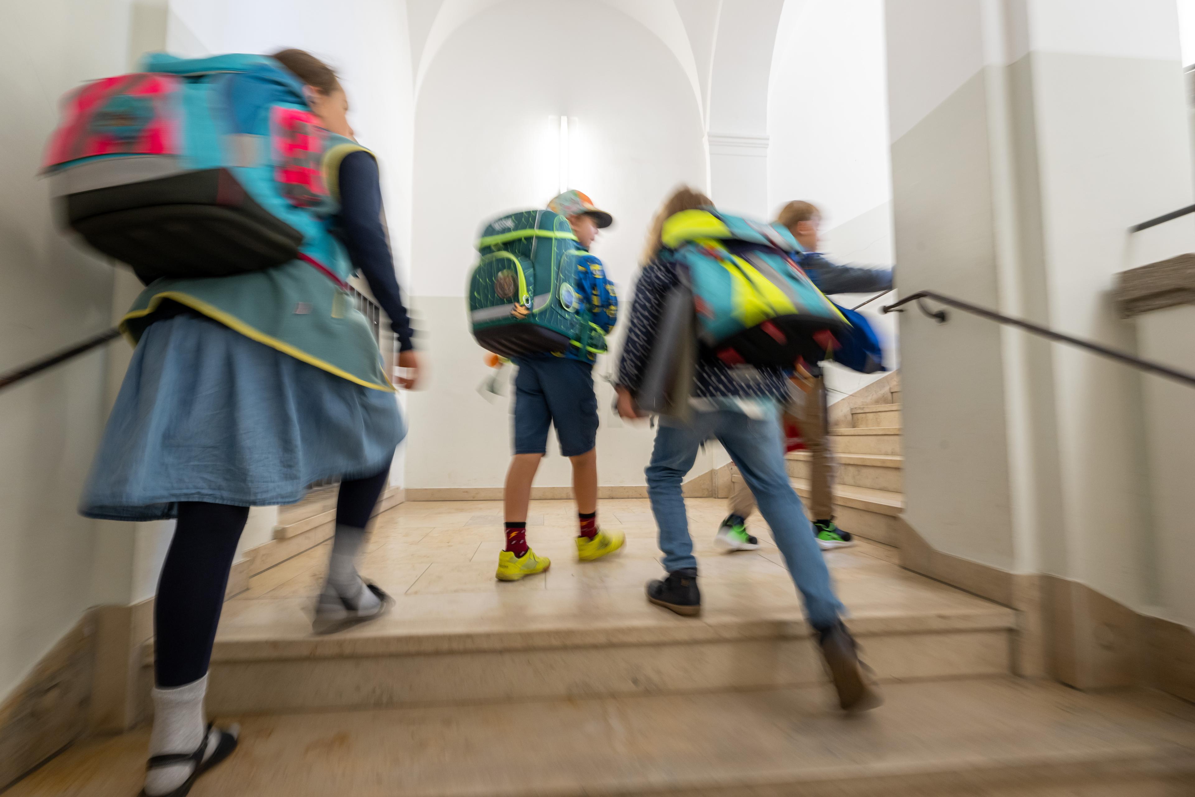 Kinder mit Schulranzen laufen am ersten Schultag die Treppe ihrer Grundschule hoch.