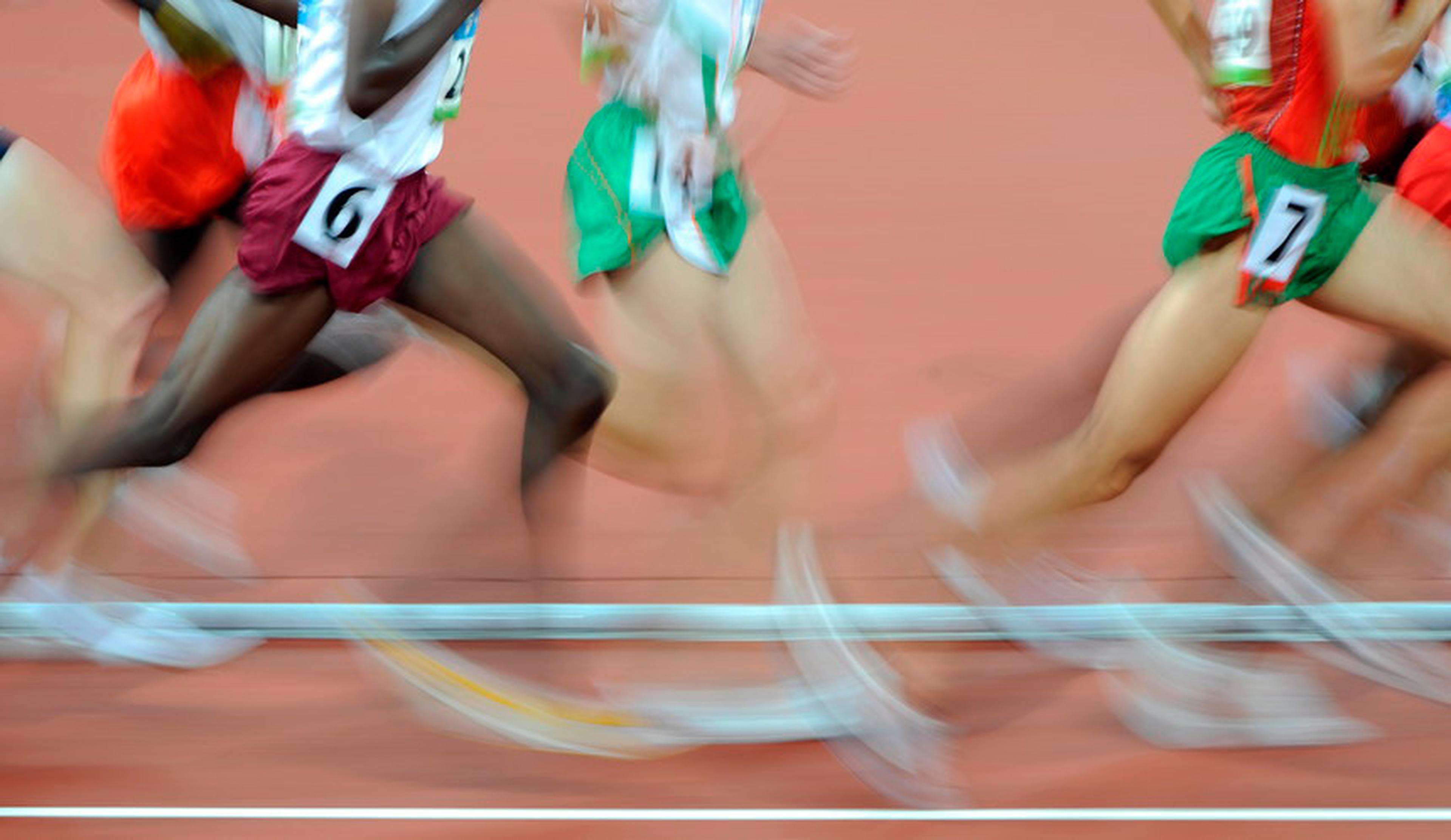 Verschwommene Beine von sprintenden Personen. Im Hintergrund eine rote Rennbahn.