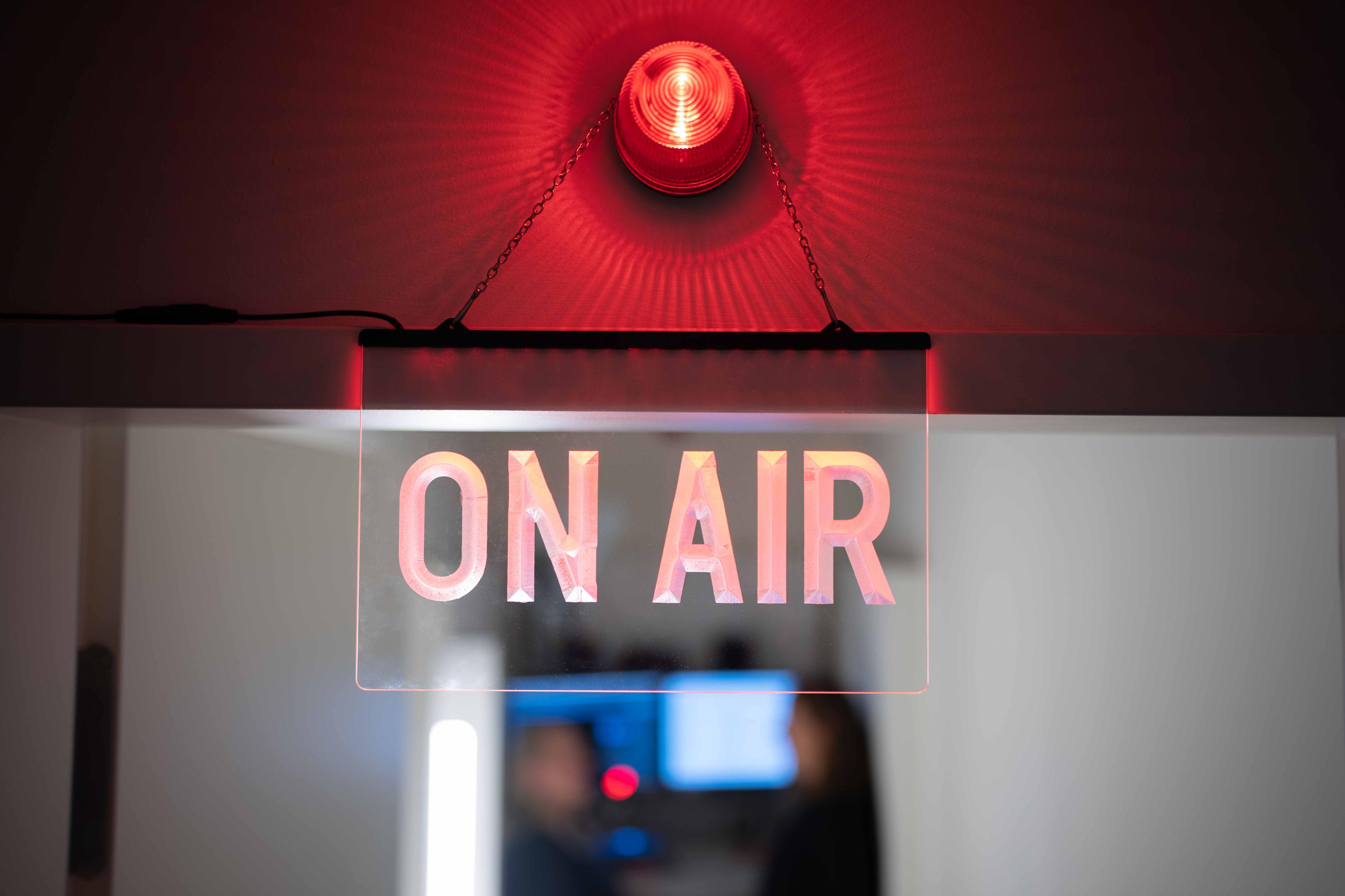 Ein Leuchtschild "On Air" hängt vor einem Tonstudio