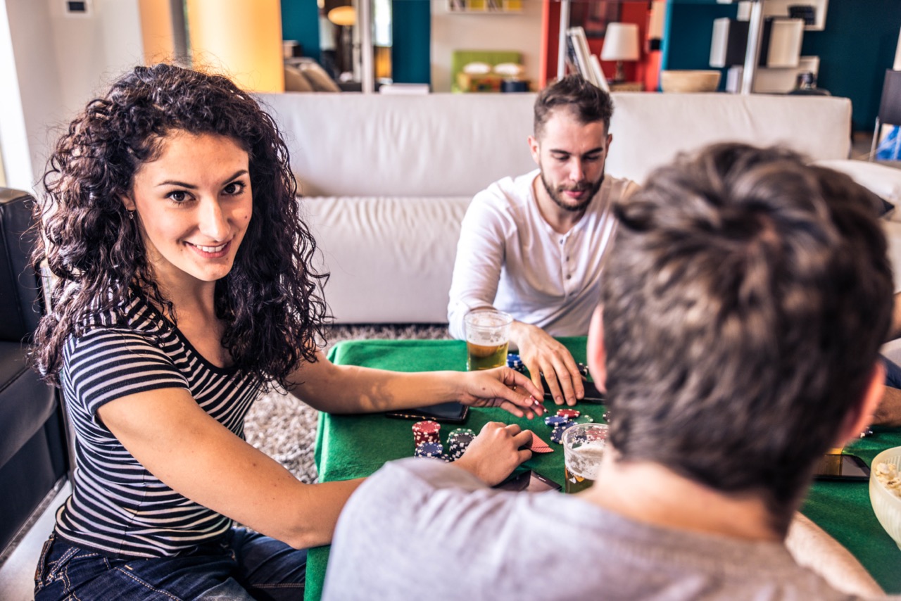 Vrouw lacht ons toe terwijl ze poker speelt met mannen en bier