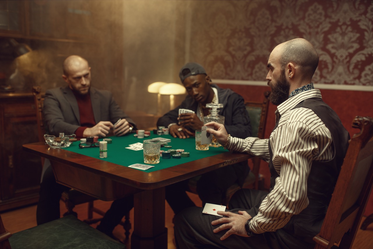 Mannen spelen poker aan een tafel, drinken alcohol en roken sigaren