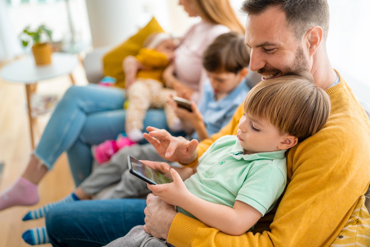 Kinderen en vader spelen op smartphone terwijl moeder baby vasthoudt