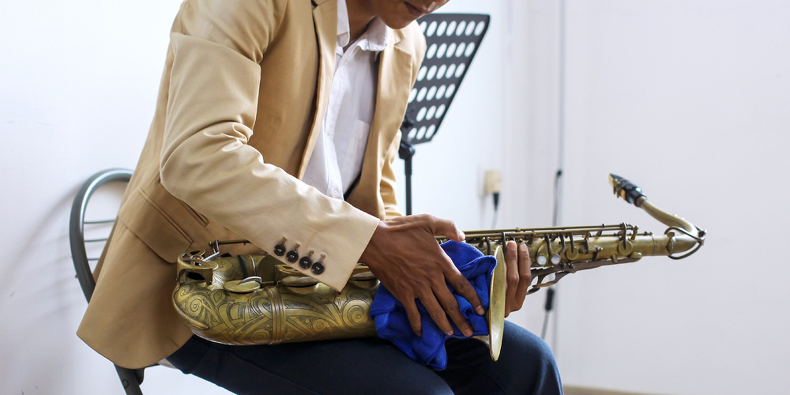 Mann hält ein goldfarbenes Saxophon mit Reinigungstuch in der Hand