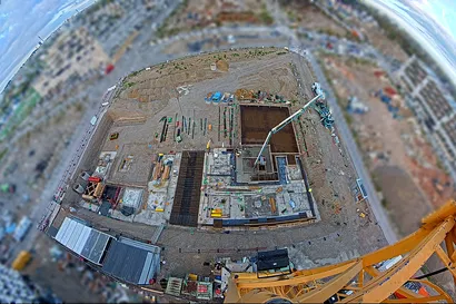 Luftaufnahme einer Baustelle mit Maschinen und Arbeitern, umgeben von einer verschwommenen städtischen Landschaft.