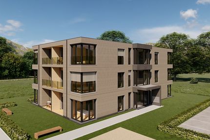 Rendering eines geplanten Mehrfamilienhauses in Holzmodulbauweise, eingebettet in einer Grünfläche und vor einem Wald.