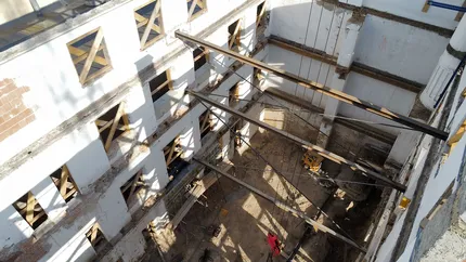 Luftaufnahme eines im Bau befindlichen Gebäudes mit einem offenen zentralen Innenhof, sichtbaren Balken, Baustellengeräten und Fensteröffnungen.