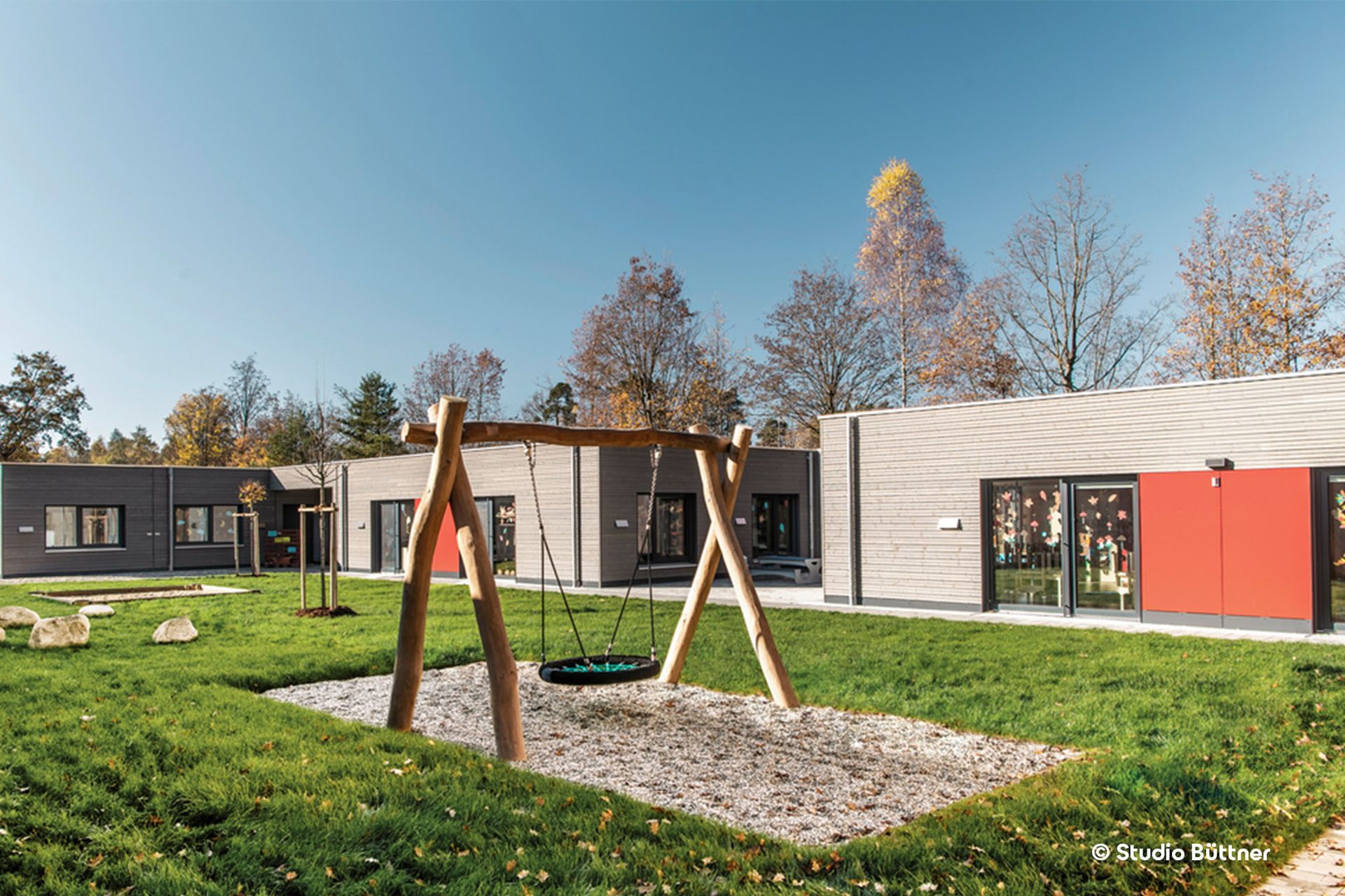 Eine Kita aus Holzmodulen mit einem Spielplatz im Vordergrund.