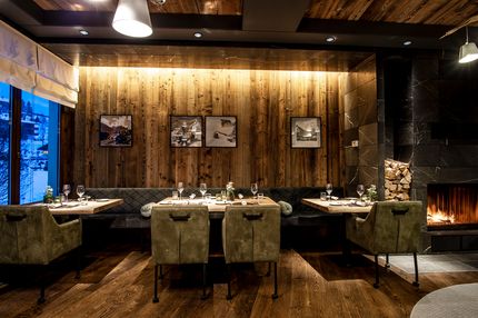 Restaurantbereich mit Holzwand, Kamin, gedeckten Tischen und gemütlicher Atmosphäre im Travel Charme Ifen Hotel in Hirschegg.