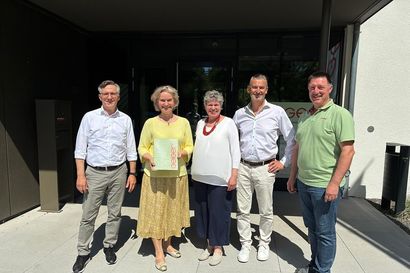 Fünf Personen stehen vor dem Niederlassungsgebäude in Augsburg mit einem unterzeichneten Vertrag.